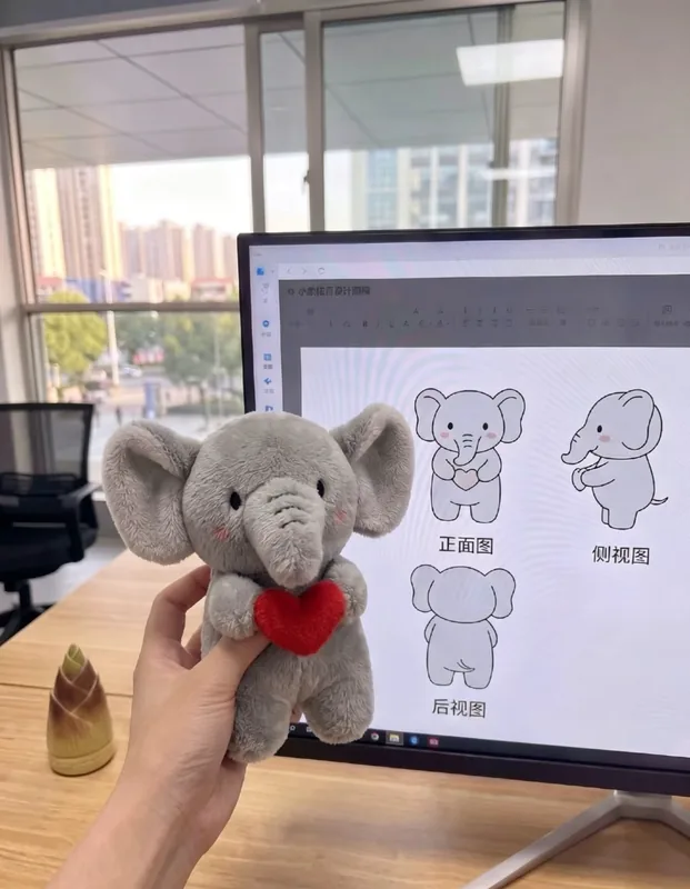 Un éléphant en peluche gris tenant un cœur rouge, à côté de dessins sur un écran.