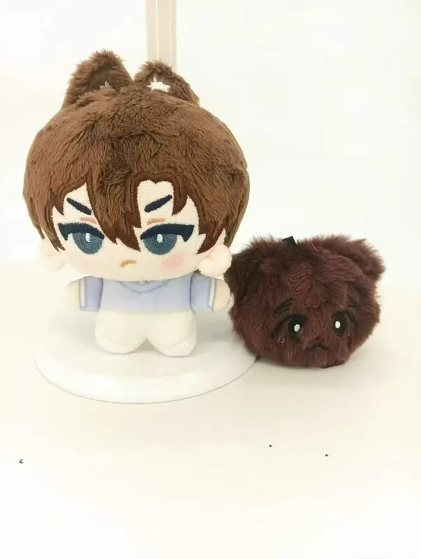 Une poupée aux cheveux bruns et aux yeux bleus à côté d'une peluche ronde brune.