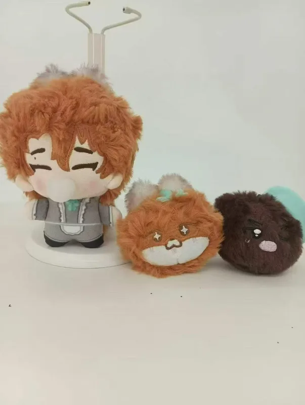 Une poupée aux cheveux orange et aux vêtements gris à côté de deux peluches rondes, orange et brun foncé.